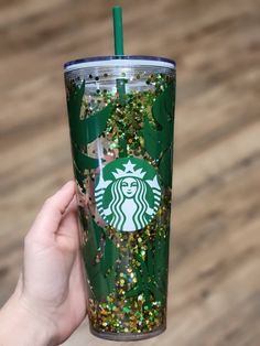 someone holding up a starbucks cup with gold and green sprinkles