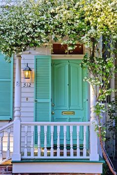 a green door on a white house with vines growing over the front and side porch