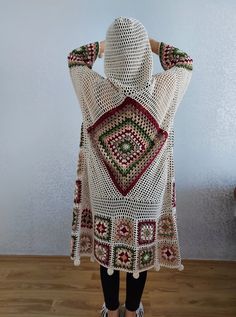 a woman wearing a white crocheted sweater and black leggings stands in front of a wall