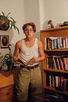 a man standing in front of a bookshelf holding a book and looking at the camera