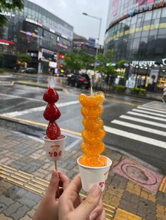 a person holding up two cups with gummy bears in them on a city street