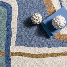 two white balls sitting on top of a blue and beige rug next to each other