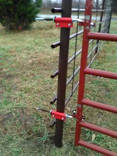 a close up of a metal fence with red bars on it and grass in the background