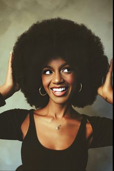 a woman with an afro smiling and holding her hair in front of her face,