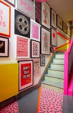 the stairs are lined with posters and framed pictures on the wall above them is a pink staircase