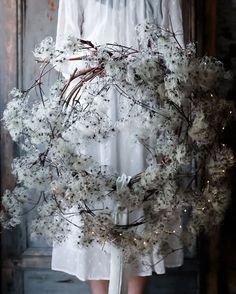 a woman in white dress holding a wreath with flowers and lights on the front door