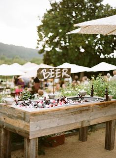 a wooden table topped with lots of plants and bottles filled with beer next to umbrellas