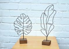 two metal sculptures on top of a wooden table next to a white brick wall,