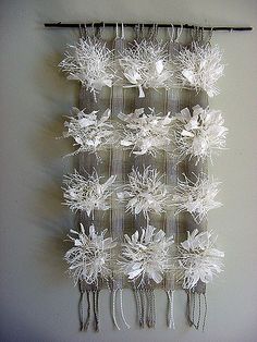 a wall hanging made out of plastic bottles and string with white flowers on the bottom