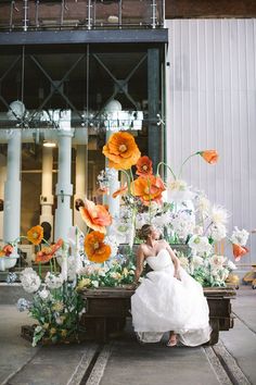 a woman in a white dress sitting on a bench with flowers and candles behind her