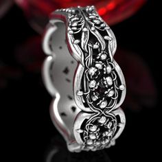 an intricately designed wedding ring sits in front of a red crystal glass ball on a black background