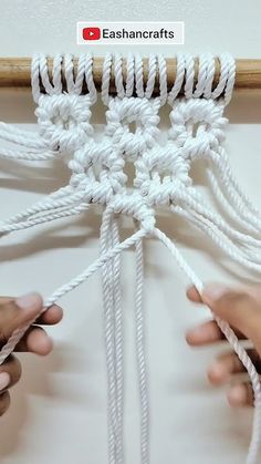 two hands are working on an art project with white yarn and wood dows, while another hand is holding the string