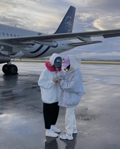 two people standing in front of an airplane on the tarmac with their hands together