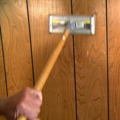 a person holding a paint roller in front of a wood paneled wall with planks