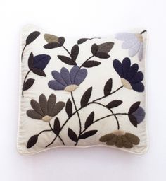 a white pillow with blue and purple flowers on it's side, sitting on a table