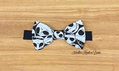 a black and white bow tie with skull designs on it, sitting on a wooden surface