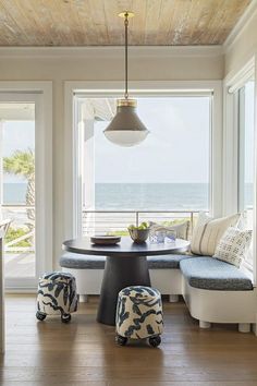 a dining room table and bench in front of large windows with ocean view on the other side