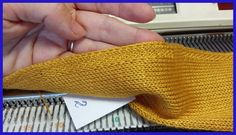 a hand holding a piece of yellow knitted material next to a sewing machine needle