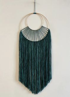 a green wall hanging with fringes and circular rings on the end, against a white wall