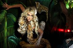 a woman with long blonde hair sitting on a stool in front of a jungle scene