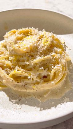 a white plate topped with pasta covered in grated cheese on top of a table