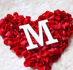 the letter m is surrounded by rose petals in a heart - shaped arrangement on a white furnishing