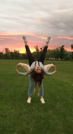 a woman is doing a handstand in the middle of a field at sunset