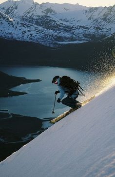 a man riding skis down the side of a snow covered slope next to a lake