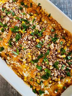 a casserole dish with corn and cheese on top, garnished with fresh herbs