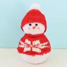 a small knitted snowman sitting on top of a white table next to a blue wall