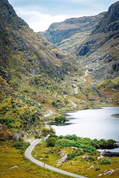 a winding road in the mountains leading to a body of water that is surrounded by greenery