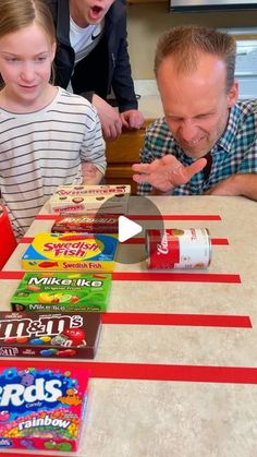 two children and an adult sitting at a table with candy bars on it, making funny faces