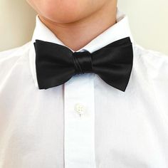 We designed this boys' black bow tie to match with our popular men's ties. The bow is pre-tied with a band collar sized for most boys from baby to 10-years old. The heavyweight woven material and smooth satin finish provide a sharp look that is suited for formal occasions. We recommend this shade for a standard black. See it in person by requesting a free color swatch. Sizing This bow tie features an adjustable band that expands to fit most babies, toddlers and children up to 10-years old. For o Solid Black Tie Bow With Ties, Solid Black Tie With Decorative Bow, Classic Solid Bow For Black-tie Events, Dapper Adjustable Satin Bow Tie, Adjustable Satin Bow Tie For Business, Adjustable Satin Bow Tie In Dapper Style, Fitted Solid Color Bow Tie For Black-tie Events, Black Bow Tie For Black-tie Events, Classic Adjustable Satin Bow Tie