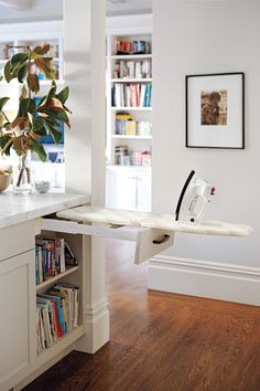 a white ironing board sitting on top of a kitchen counter next to a book shelf