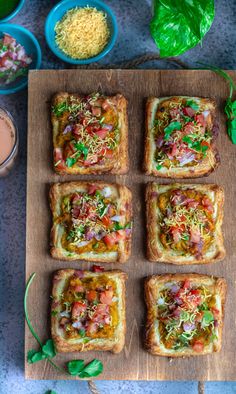 several square pieces of bread with various toppings on it and some dipping sauce next to them