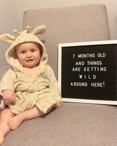 a baby in a giraffe robe sitting next to a sign