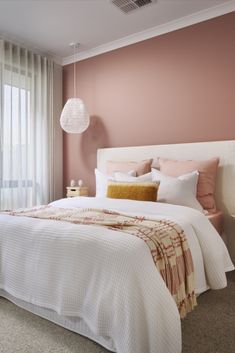 a bedroom with pink walls and white bedspread on the bed in front of a window