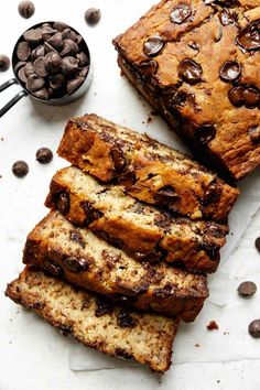 sliced loaf of chocolate chip banana bread on a white surface next to a bowl of chocolate chips