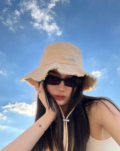 a woman wearing a tan hat and sunglasses with her hands on her head in front of the sky