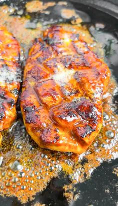 two meat patties cooking in a skillet with oil on them and some seasoning sprinkles