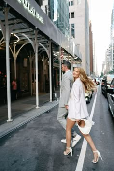 a man and woman walking down the street in front of a building with tall buildings