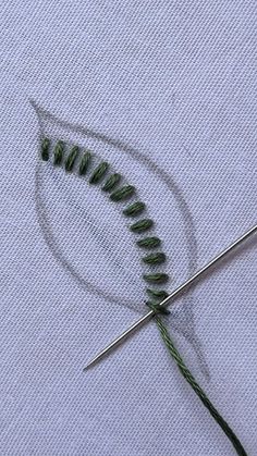 the needle is being used to sew some green thread on a white piece of cloth