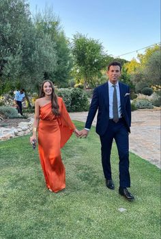 a man and woman in formal wear holding hands walking on grass with trees in the background