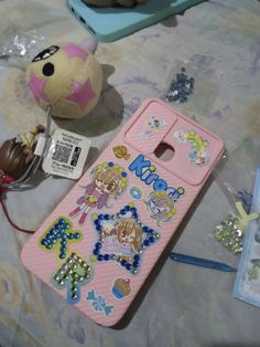 a pink cell phone sitting on top of a bed next to a stuffed animal and other items