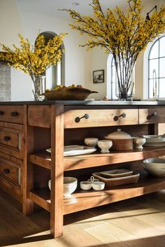 a kitchen island with plates and bowls on it in front of a window filled with yellow flowers