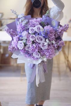 a woman holding a bouquet of purple flowers in her right hand and a camera behind her head