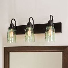 three mason jar lights are mounted on the wall above a mirror and light fixture in a bathroom