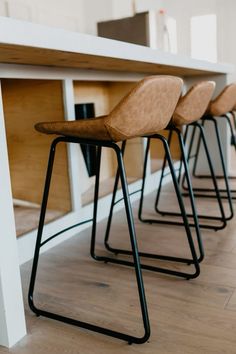 three stools sitting on top of a wooden floor next to a white countertop