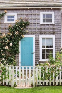 a white picket fence in front of a gray house with blue door and window frames