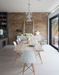 a wooden table with white chairs and plates on it in front of a brick wall